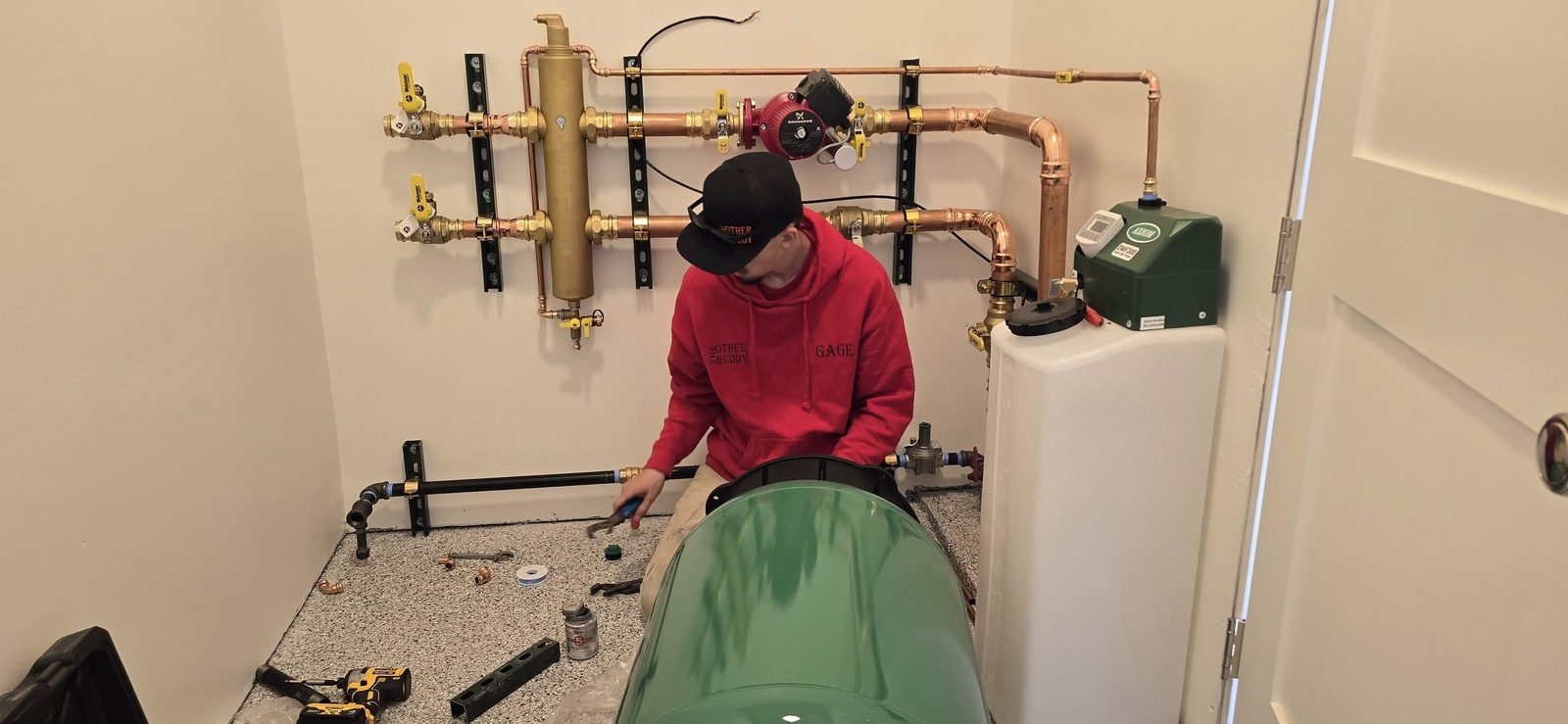Technician working on a hydronic distribution install with copper manifold, Grundfos circulator, dirt separator, and Webstone shutoff valves