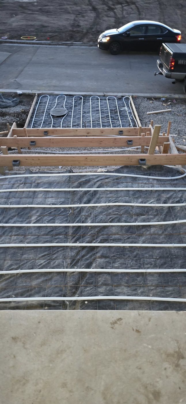 Snow-melt install in progress showing PEX tubing tied to rebar grid over vapor barrier, before concrete pour